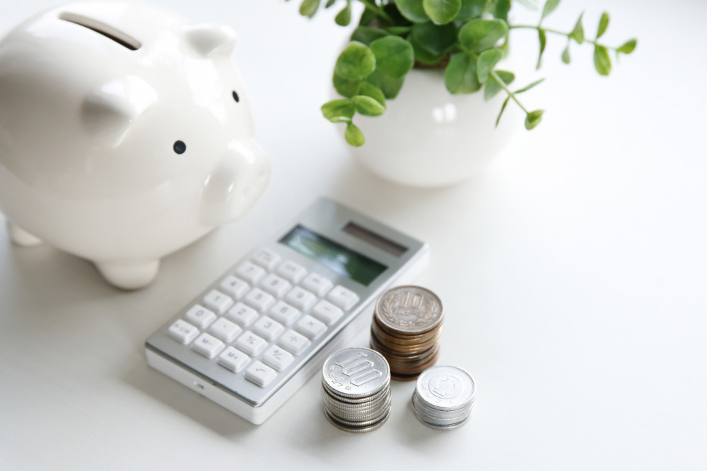 white piggy bank with calculator, coins and white vase in front of it