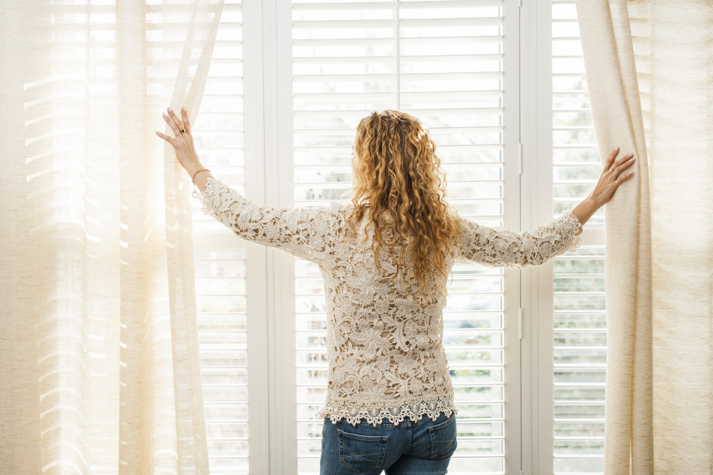 A woman opening sheer curtains in a window